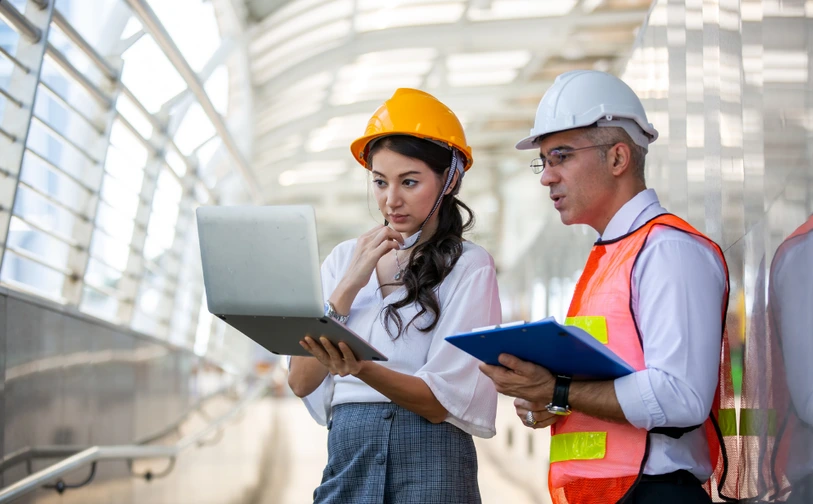 Stratégie Performance Énergétique : Audit et Optimisation Deux professionnels en tenue de chantier analysant des données sur ordinateur et tablette pour élaborer une stratégie de performance énergétique